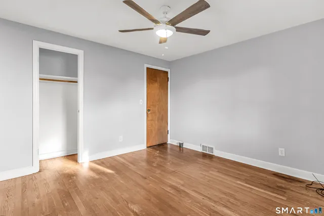 an empty room with wooden floor and a ceiling fan