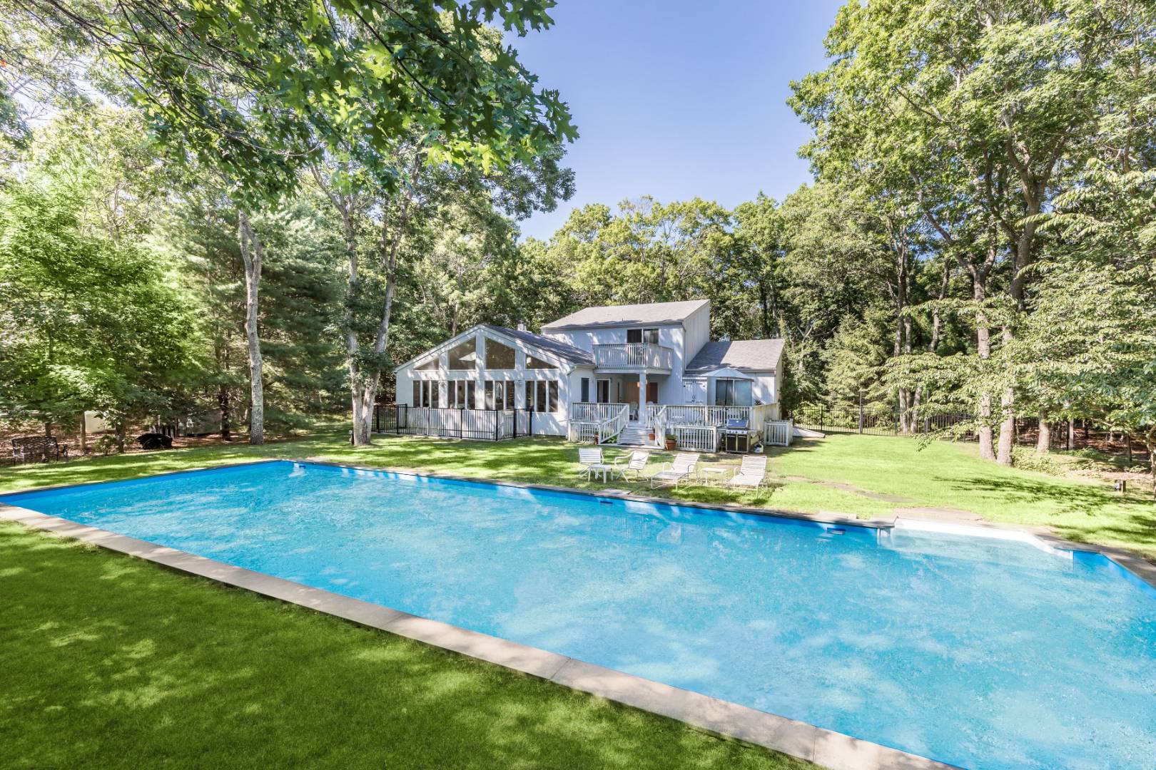 a view of a swimming pool with lawn chairs and large trees