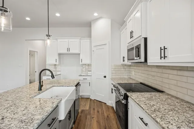 a large kitchen with stainless steel appliances granite countertop a sink a window and white cabinets