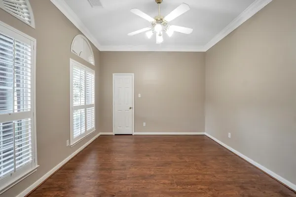 an empty room with wooden floor fan and windows