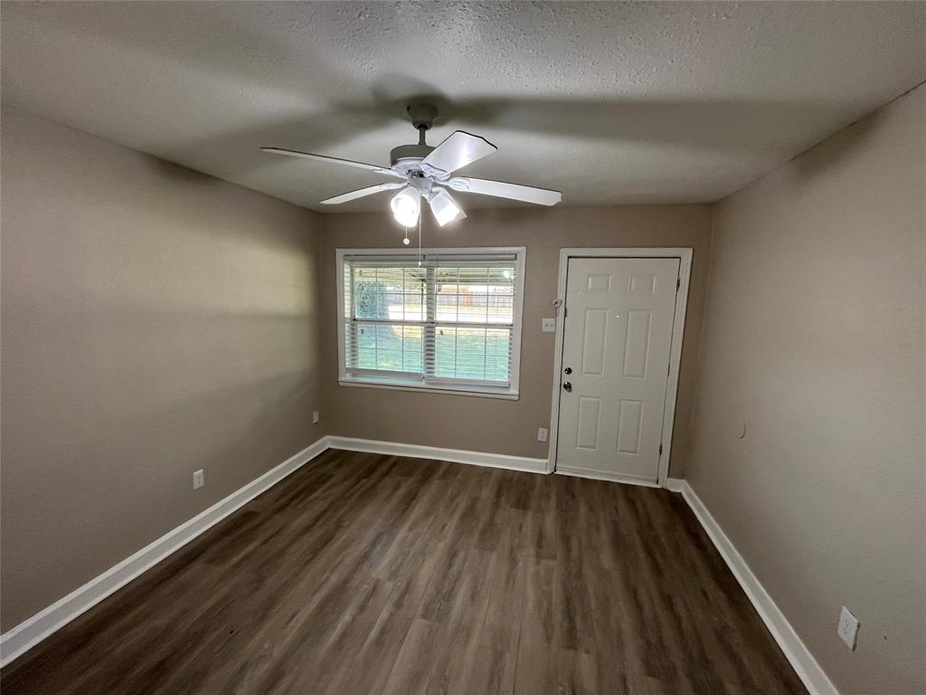 1316 North Prairie Creek Road Dallas, TX 75217 - Photo 4 of 19 Spacious room featuring wood-finish flooring, a ceiling fan with integrated lighting, a window with horizontal blinds, a paneled entry door, and painted walls with white trim