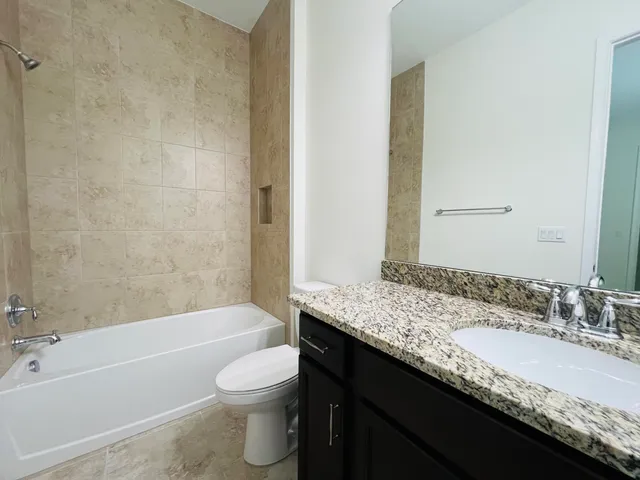 a bathroom with a granite countertop bathtub sink vanity mirror and toilet
