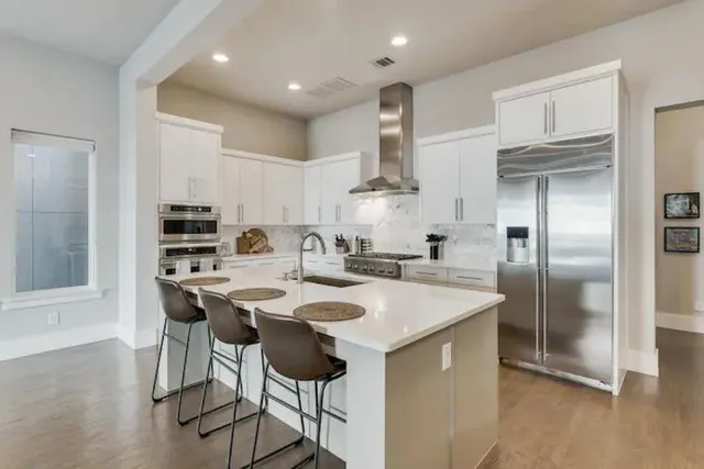 a kitchen with stainless steel appliances granite countertop a sink a stove a refrigerator and island with wooden floor