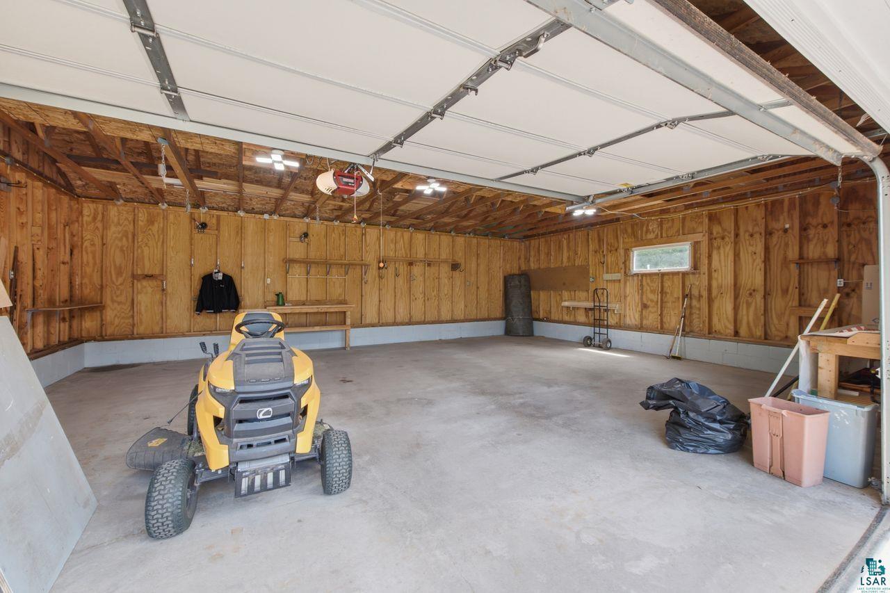61018 Dahlstrom Road Ashland, WI 54806 - Photo 19 of 28 Spacious garage featuring a concrete floor, wood-paneled walls, multiple built-in shelves, and natural light from a horizontal window