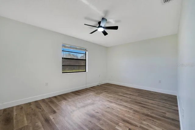 an empty room with wooden floor ceiling fan and windows