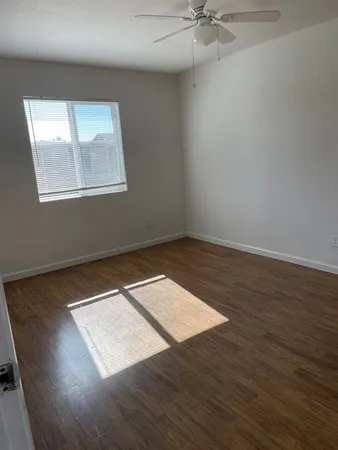 an empty room with wooden floor chandelier fan and windows