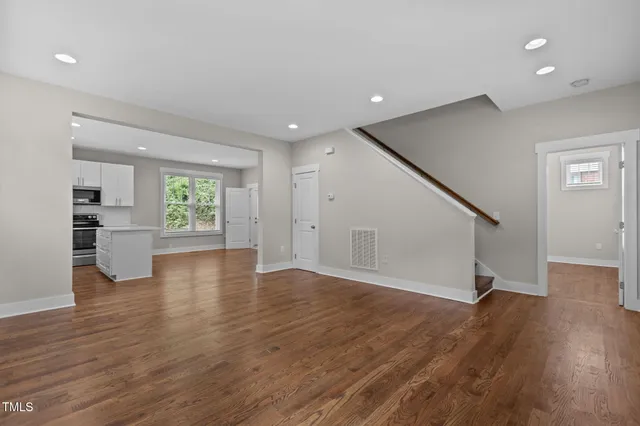 a view of empty room with wooden floor and kitchen