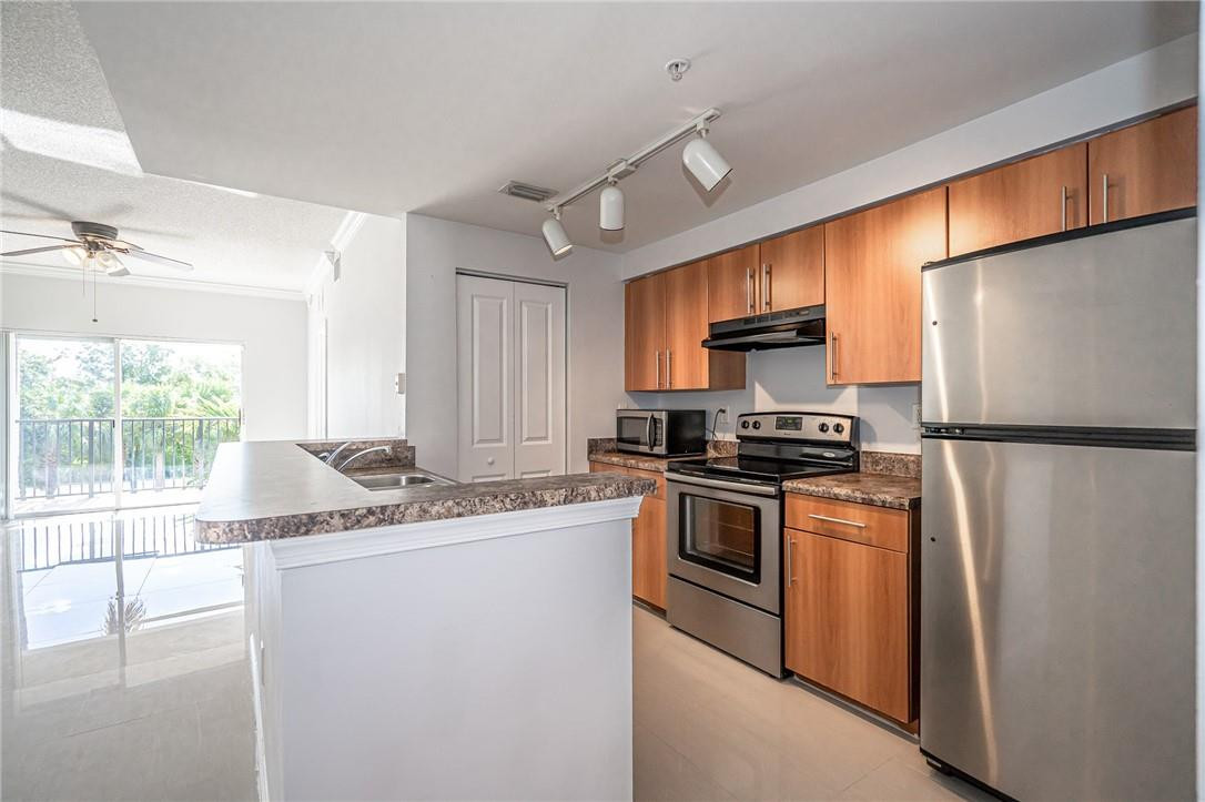 5860 West Sample Road, Unit 304 Coral Springs, FL 33067 - Photo 7 of 22 a kitchen with stainless steel appliances granite countertop a refrigerator a sink dishwasher a stove and white countertops with wooden floor