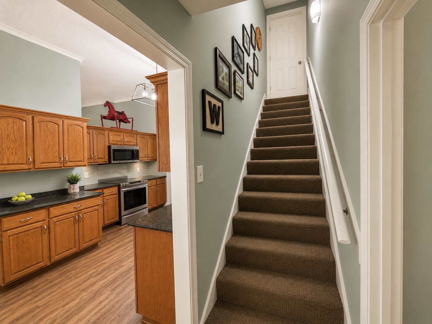 1946 Little John Road Millington, TN 38053 - Photo 8 of 20 Carpeted staircase with white handrail and a doorway opening to a kitchen featuring wood-finish cabinetry, dark countertops, and stainless steel appliances