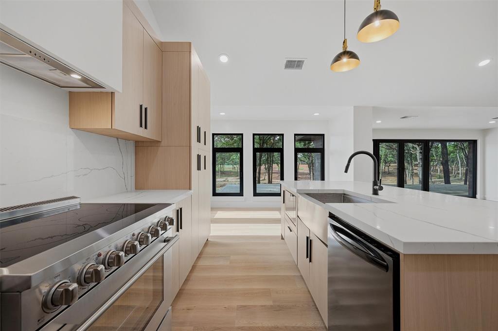 410 Arkansas Road Sadler, TX 76264 - Photo 13 of 40 Modern kitchen featuring a stainless steel range with hood, light wood-finish cabinetry, a large kitchen island with a stainless steel farmhouse sink, and a black gooseneck faucet