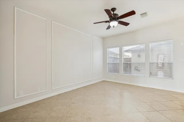 an empty room with chandelier fan and windows