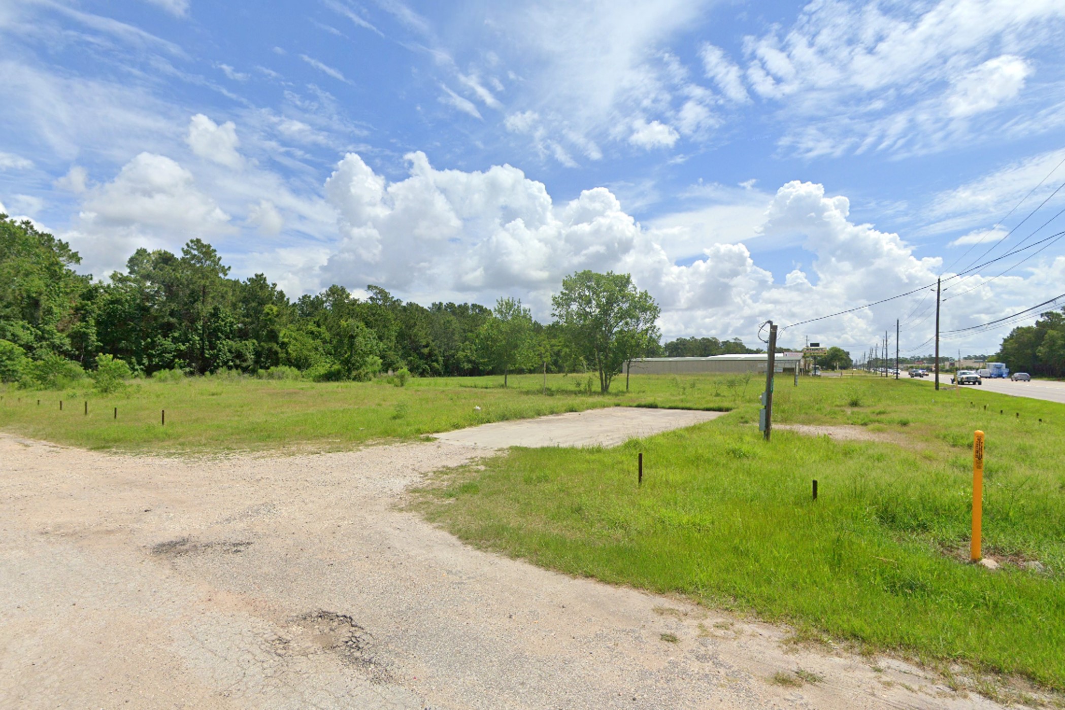 4855 Atascocita Road Humble, TX 77346 - Photo 4 of 6 This photo shows a spacious, open plot of land with grassy areas, surrounded by trees. It's adjacent to a road with light traffic, offering potential for development or a private retreat.