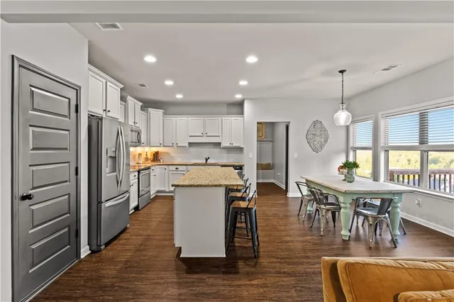 a kitchen with stainless steel appliances granite countertop a refrigerator a stove top oven a dining table and chairs with wooden floor