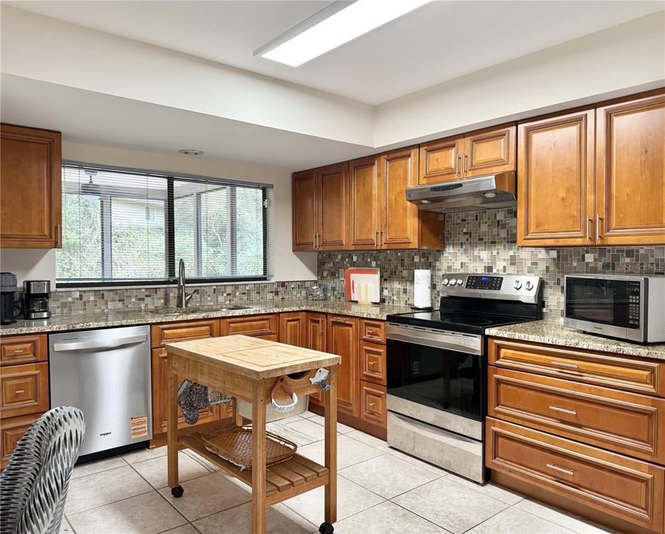 6101 Soaring Avenue Temple Terrace, FL 33617 - Photo 11 of 53 a kitchen with stainless steel appliances granite countertop a stove top oven a sink dishwasher and chairs with wooden floor