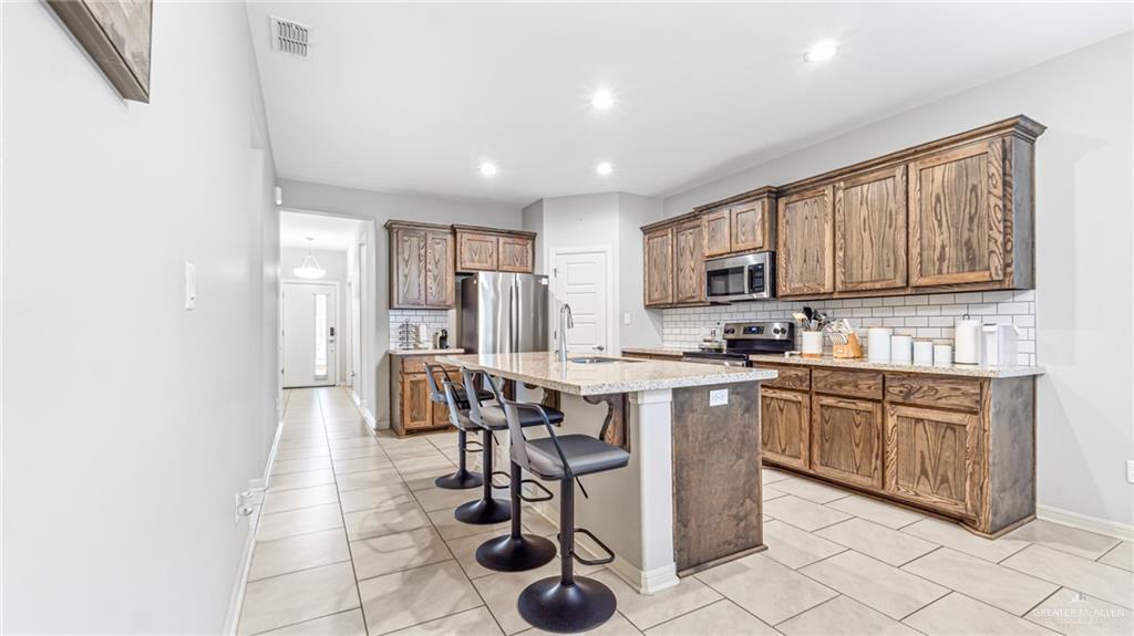14208 Boykin Creek Road McAllen, TX 78504 - Photo 6 of 30 a kitchen with stainless steel appliances granite countertop a stove a sink dishwasher and a refrigerator with wooden cabinets