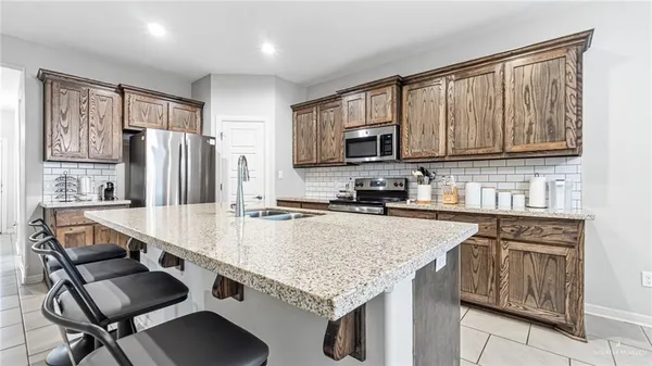 a kitchen with stainless steel appliances granite countertop a stove top oven a sink dishwasher and a refrigerator with wooden cabinets