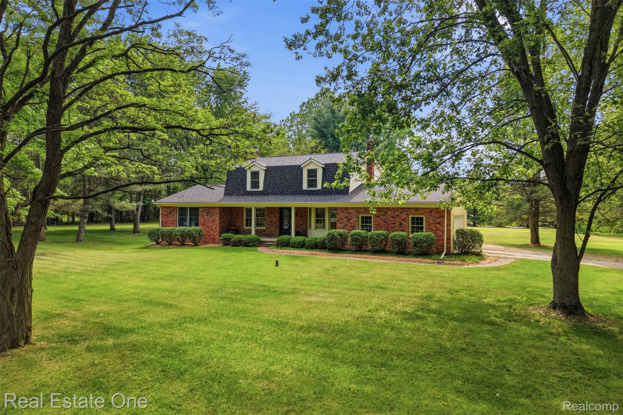 1765 Rowe Road Milford, MI 48380 - Photo 48 of 61 Brick ranch home featuring a dormer roofline with two windows, a dark shingle roof, and a mature tree-lined green lawn