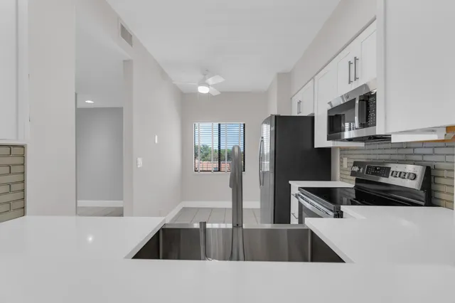 a kitchen with stainless steel appliances a sink a stove a microwave a sink a refrigerator white cabinets and wooden floor