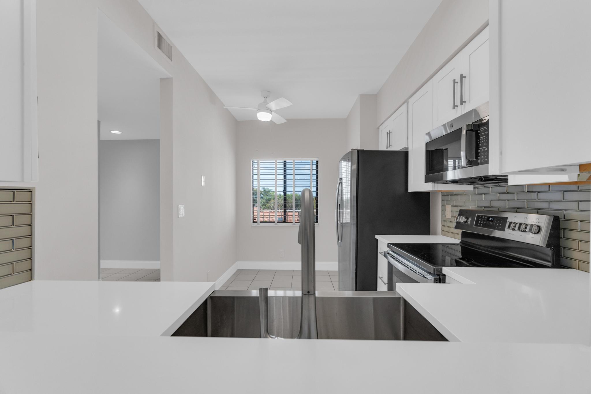 a kitchen with stainless steel appliances a sink a stove a microwave a sink a refrigerator white cabinets and wooden floor