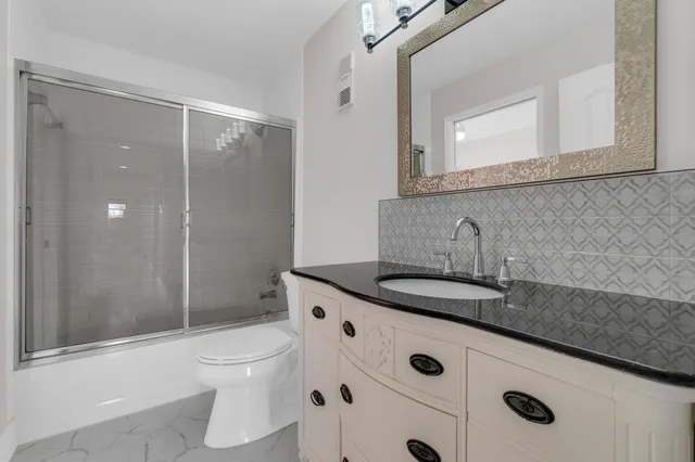 a bathroom with a granite countertop sink a toilet a mirror and shower