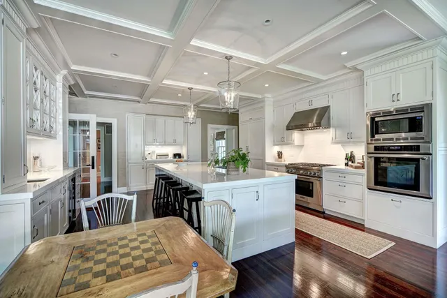 a kitchen with stainless steel appliances granite countertop a stove a refrigerator a kitchen island a dining table and chairs with wooden floor