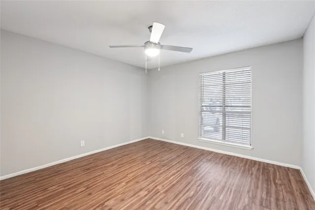 an empty room with wooden floor chandelier fan and windows