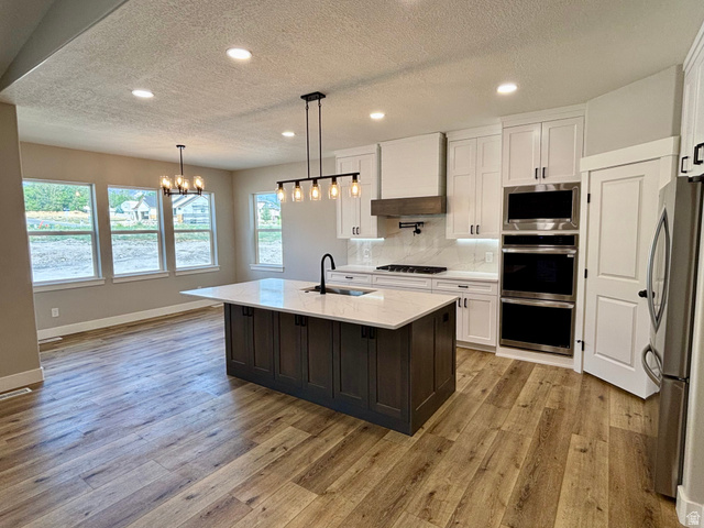 1184 West 3250 North Ogden, UT 84414 - Photo 10 of 69 Kitchen featuring a central island with a light-toned quartz countertop, white cabinetry, integrated stainless steel appliances, lvp wood style flooring, recessed lighting and dining/kitchen island lighting