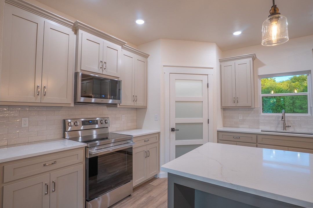 205 Blessings Way Colbert, OK 74733 - Photo 10 of 24 Modern kitchen featuring stainless steel appliances, light-toned cabinetry, white countertops, a subway tile backsplash, and wood-finish flooring