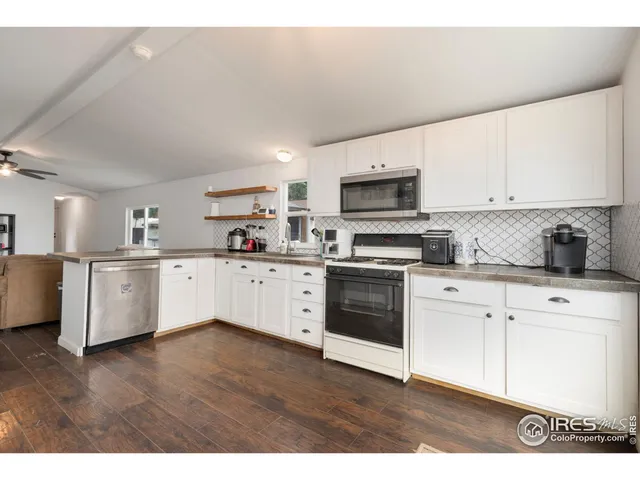 a kitchen with stainless steel appliances granite countertop a sink a stove a microwave a refrigerator a white cabinets and wooden floor