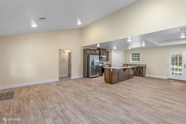 a large room with stainless steel appliances a large kitchen counter top a wooden floor and windows