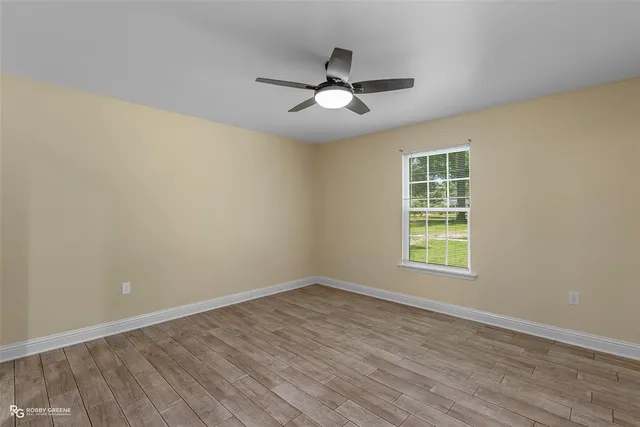 an empty room with wooden floor ceiling fan and windows