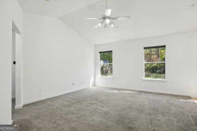 an empty room with chandelier fan and windows