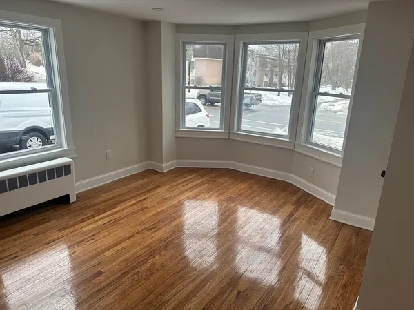 a view of an empty room with wooden floor and windows