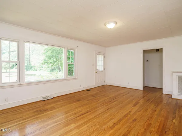 a view of an empty room with wooden floor and a window