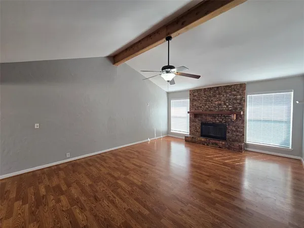 a view of an empty room with wooden floor fireplace and a window