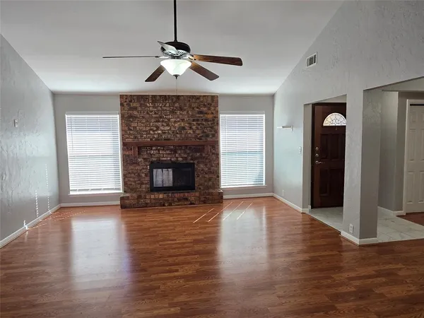 a view of an empty room with wooden floor fireplace and a window