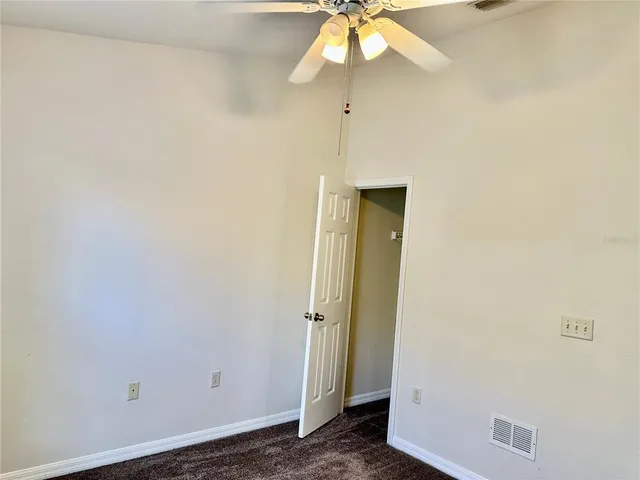 an empty room with chandelier fan and windows