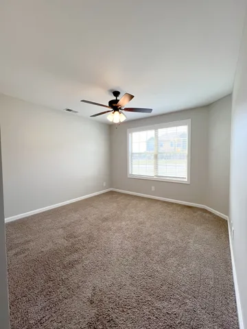 an empty room with ceiling fan and windows