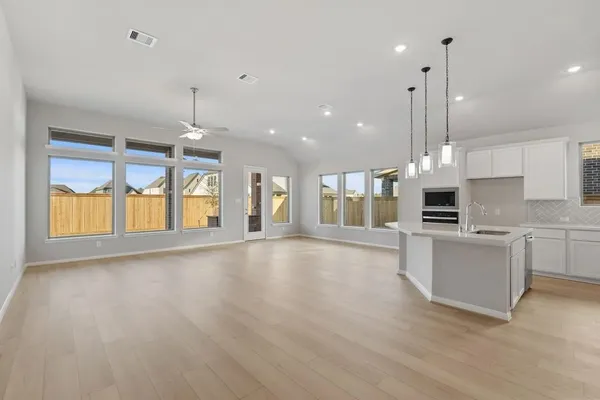 a view of an empty room with kitchen and window