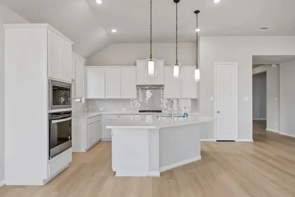 a kitchen with stainless steel appliances granite countertop a sink a stove a refrigerator and white cabinets with wooden floor