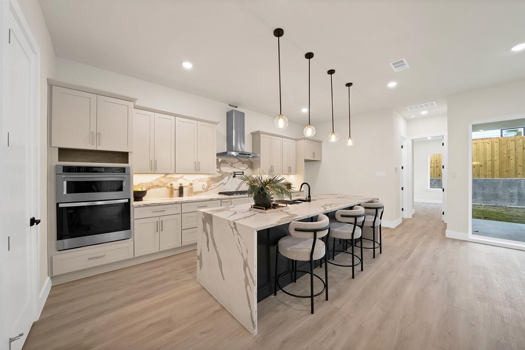 1415 Fayette Street Dallas, TX 75203 - Photo 16 of 40 Gourmet kitchen featuring a large waterfall island, stainless steel double ovens, a built-in range hood, light wood-finish flooring, and pendant lighting