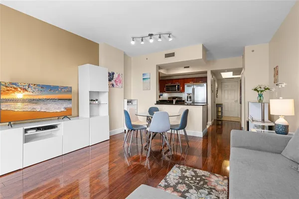 a living room with stainless steel appliances furniture wooden floor and a kitchen view