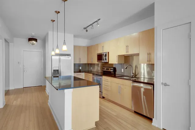 a kitchen with stainless steel appliances granite countertop a refrigerator a sink dishwasher a stove and white countertops with wooden floor