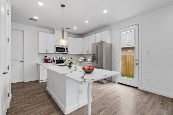 a kitchen with stainless steel appliances kitchen island granite countertop a refrigerator a stove top oven a sink and dishwasher with wooden floor