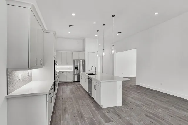 a large white kitchen with wooden floor and stainless steel appliances