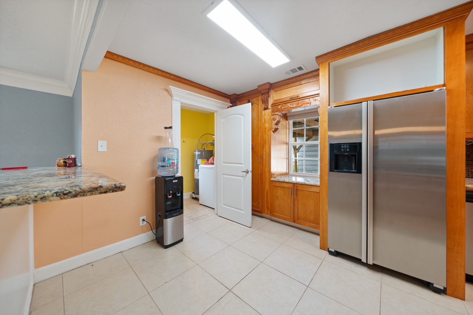 6742 Dusty Lane Conroe, TX 77306 - Photo 13 of 33 Bright kitchen area with tile flooring, featuring a stainless steel refrigerator and ample wood cabinetry. A granite countertop breakfast bar adds functionality, and a doorway leads to the laundry room.