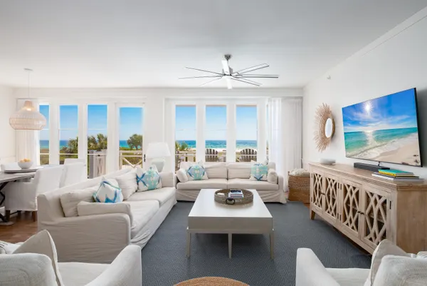 a living room with furniture two large window and a flat screen tv