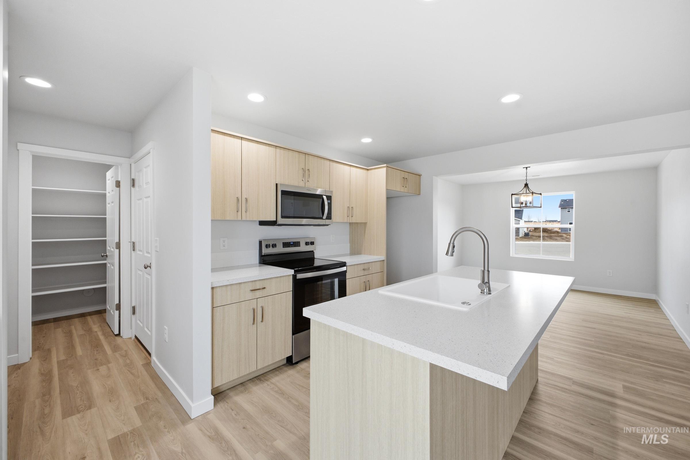 13718 Inman Court Caldwell, ID 83607 - Photo 6 of 20 Kitchen featuring stainless steel appliances, light wood finish cabinets, a center island with sink, light wood-type flooring, and pendant lighting