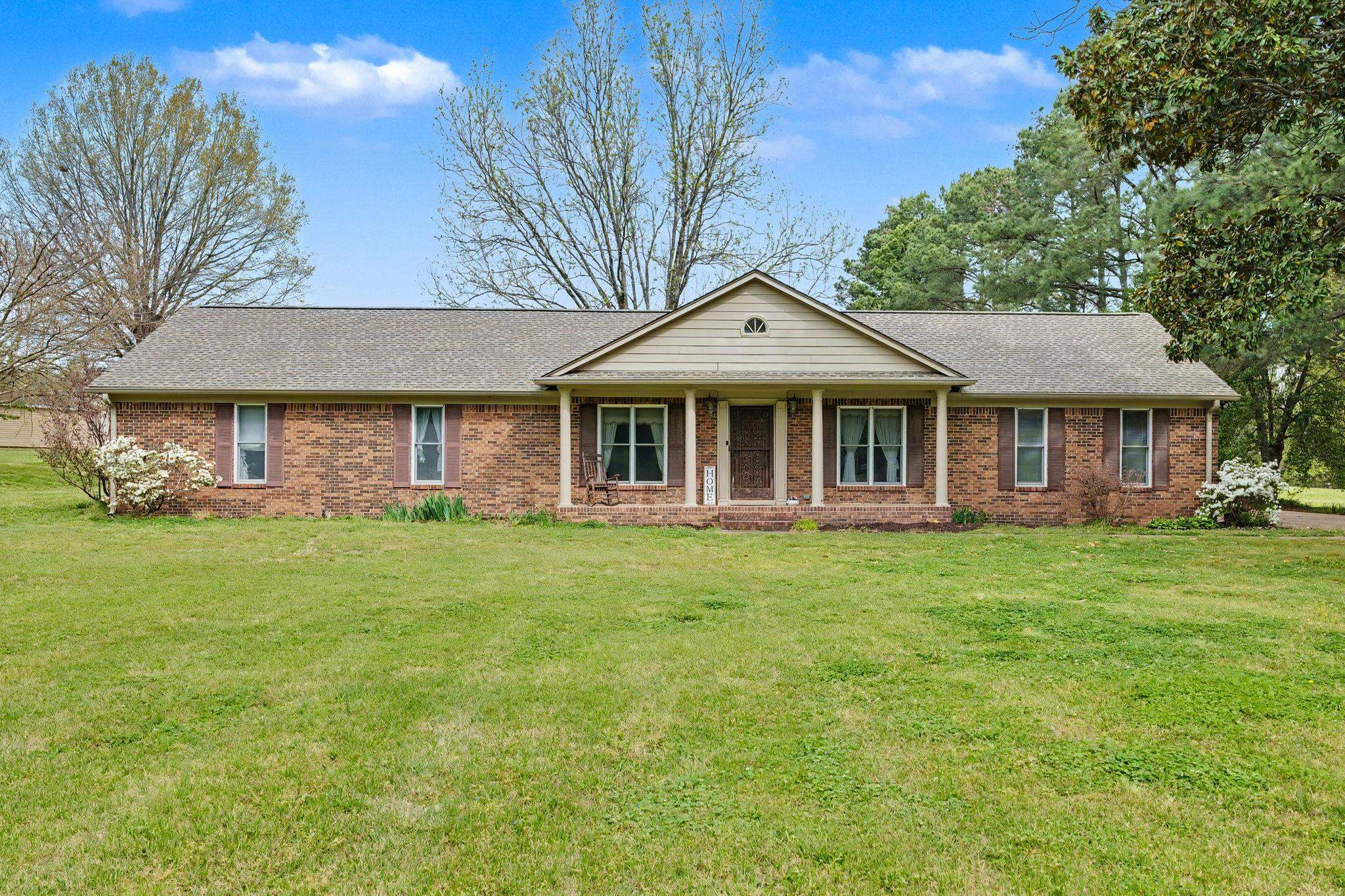 Single story home with a shingled roof, covered porch, a front yard, and brick siding