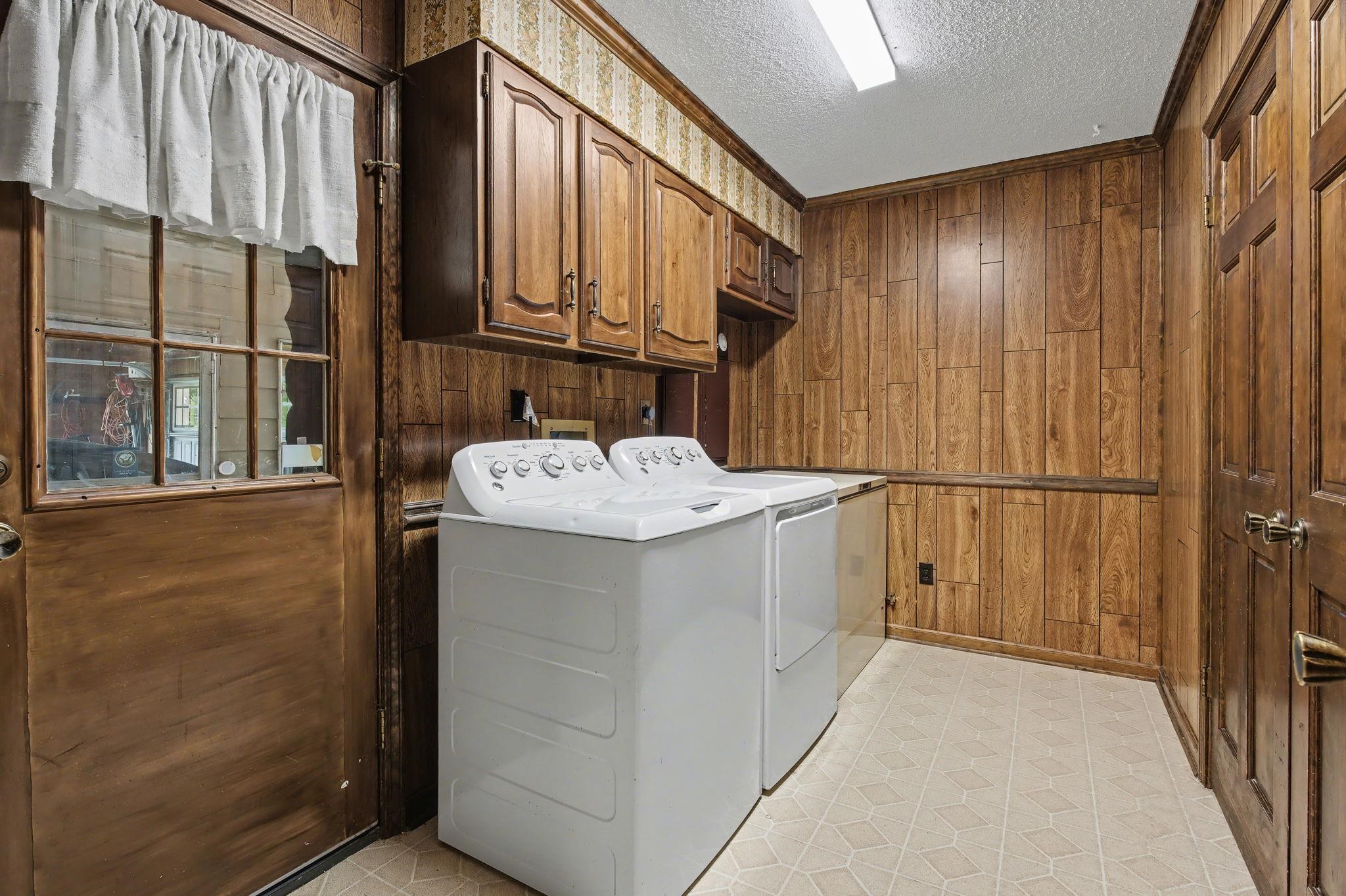 11380 Sycamore Farms Road Collierville, TN 38017 - Photo 19 of 38 Laundry area featuring wood walls, a textured ceiling, washing machine and clothes dryer, light flooring, and cabinet space